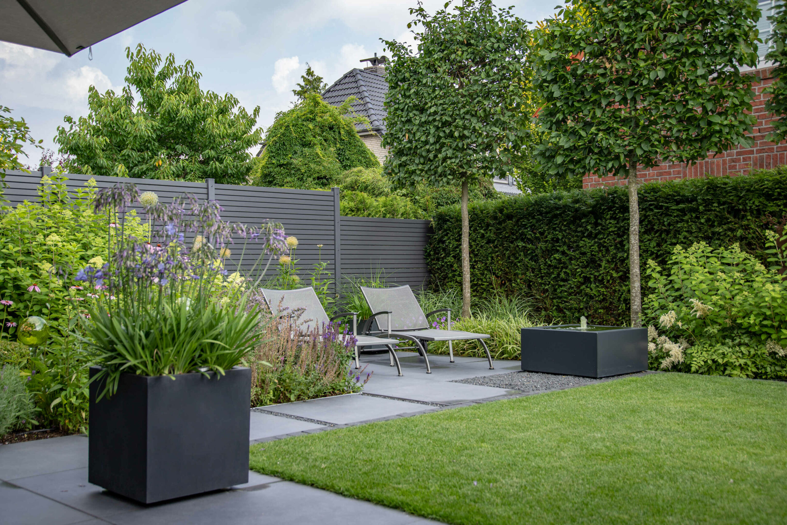 Gartenbereich mit zwei Liegen, einer Pflanzenschale und gepflegten Pflanzen in einem modernen Design.