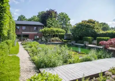 Schwimmteich mit Holzsteg und Staudenbeet in einem Gartenbereich.