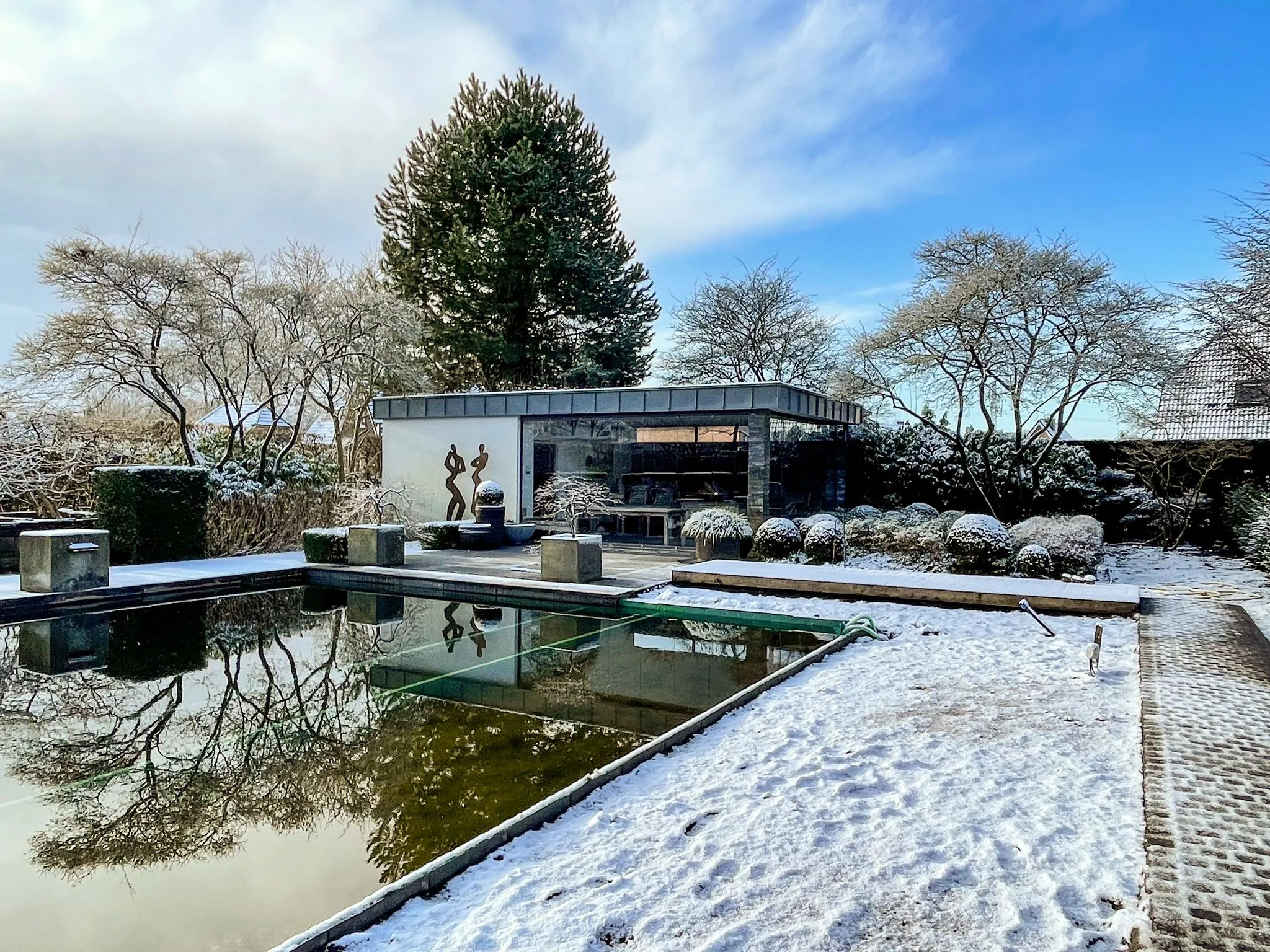 Modernes Gebäude mit Glasfront und Winterlandschaft, umgeben von schneebedeckten Bäumen und einem Teich.