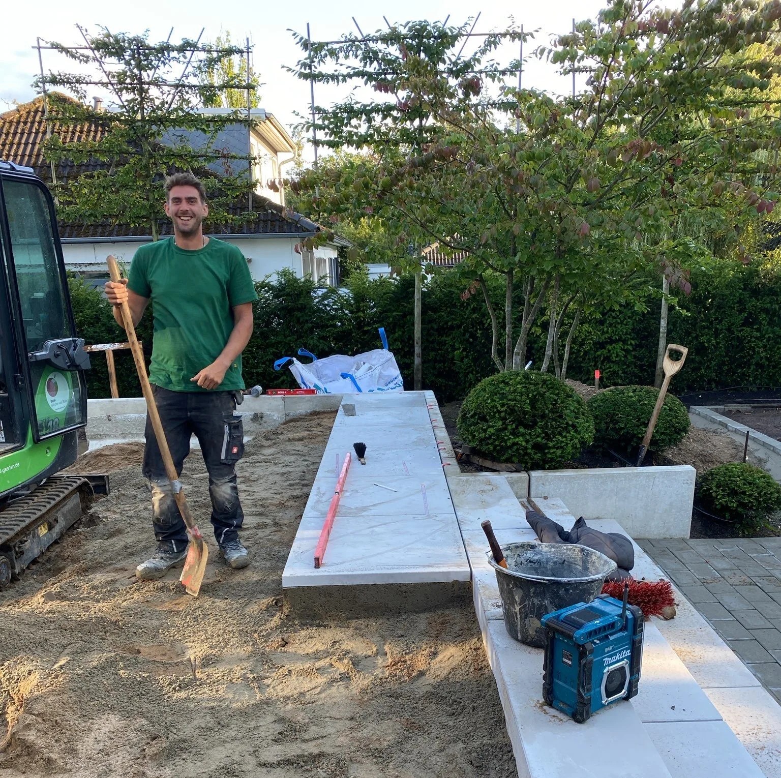 Mitarbeiter auf Baustelle mit Werkzeug Ein Mitarbeiter steht auf einer Baustelle mit einer Schaufel in der Hand und Werkzeugen in der Nähe.